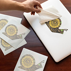 Snail decal being applied to a laptop with extra decals waiting nearby.